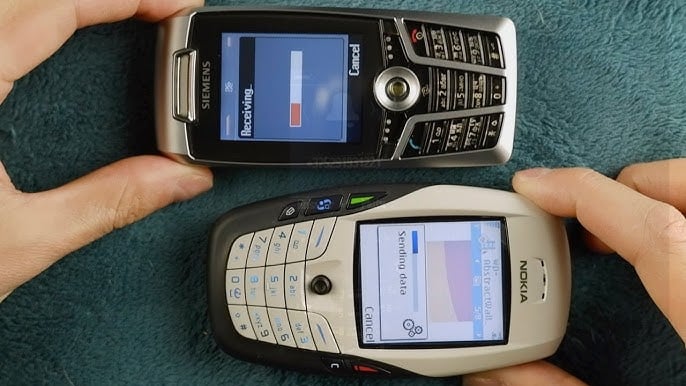 nokia (A close-up photograph of two vintage mobile phones, a Siemens and a Nokia, placed side-by-side on a textured blue surface. The Siemens phone displays a 'Receiving...' progress bar, while the Nokia phone shows a 'Sending data' screen, illustrating a legacy infrared (IrDA) data transfer between devices.")